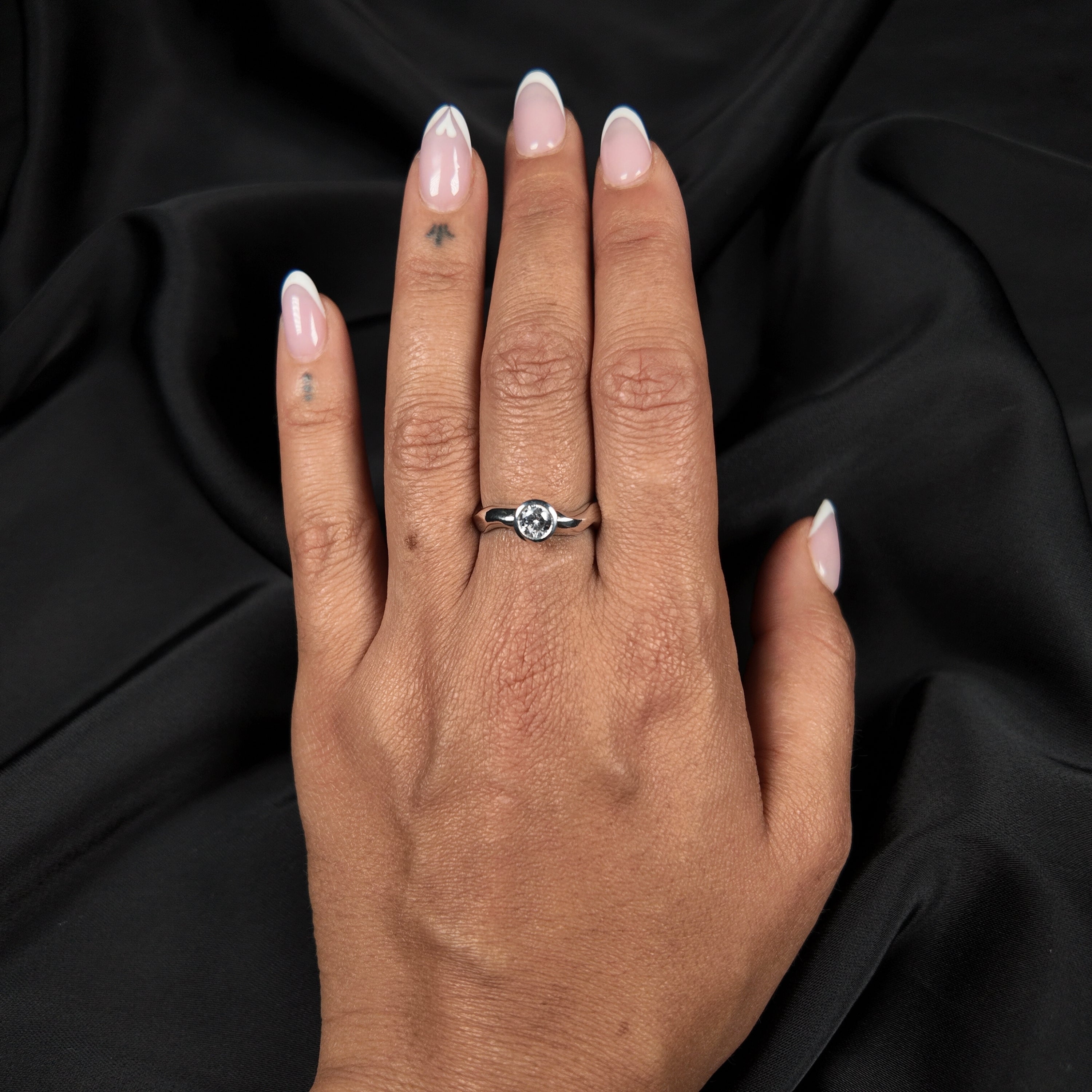 Hand wearing a silver cubic zirconia gemstone ring against a black background