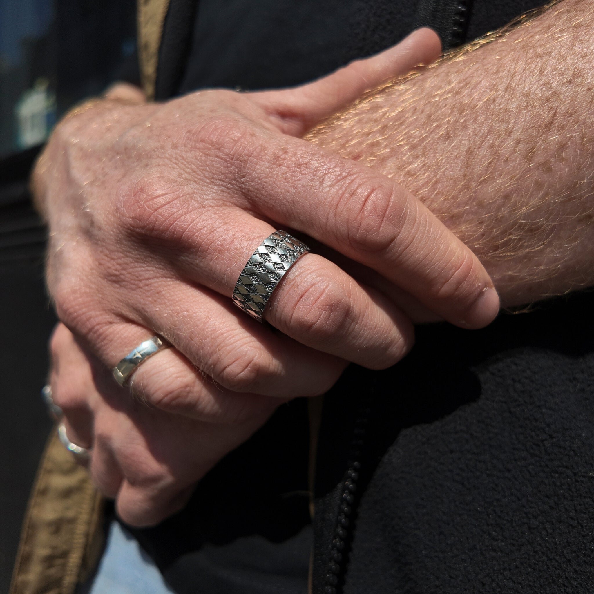 Chequered silver square ring with oxidised finish on hand with hand holding wrist