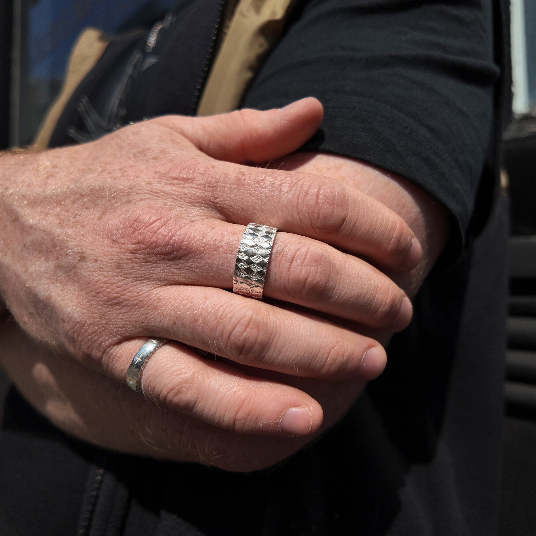 Chequered silver square ring with polished finish on hand with hand holding opposite arm