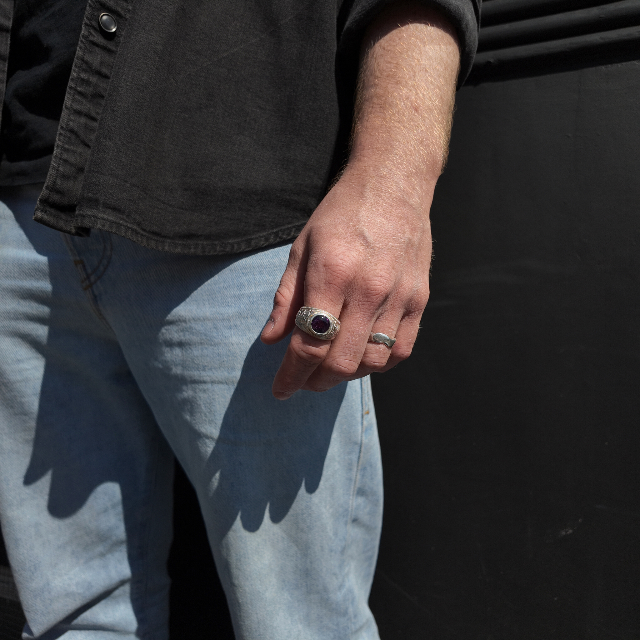 Gun engraved college signet ring with amethyst on hand by waist