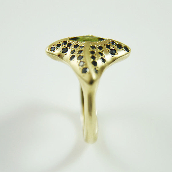 The ring features a central marquise green tourmaline and 50pts of black diamonds on each wing plate to maximise sparkle from every angle. Hand-crafted in 9ct yellow gold.