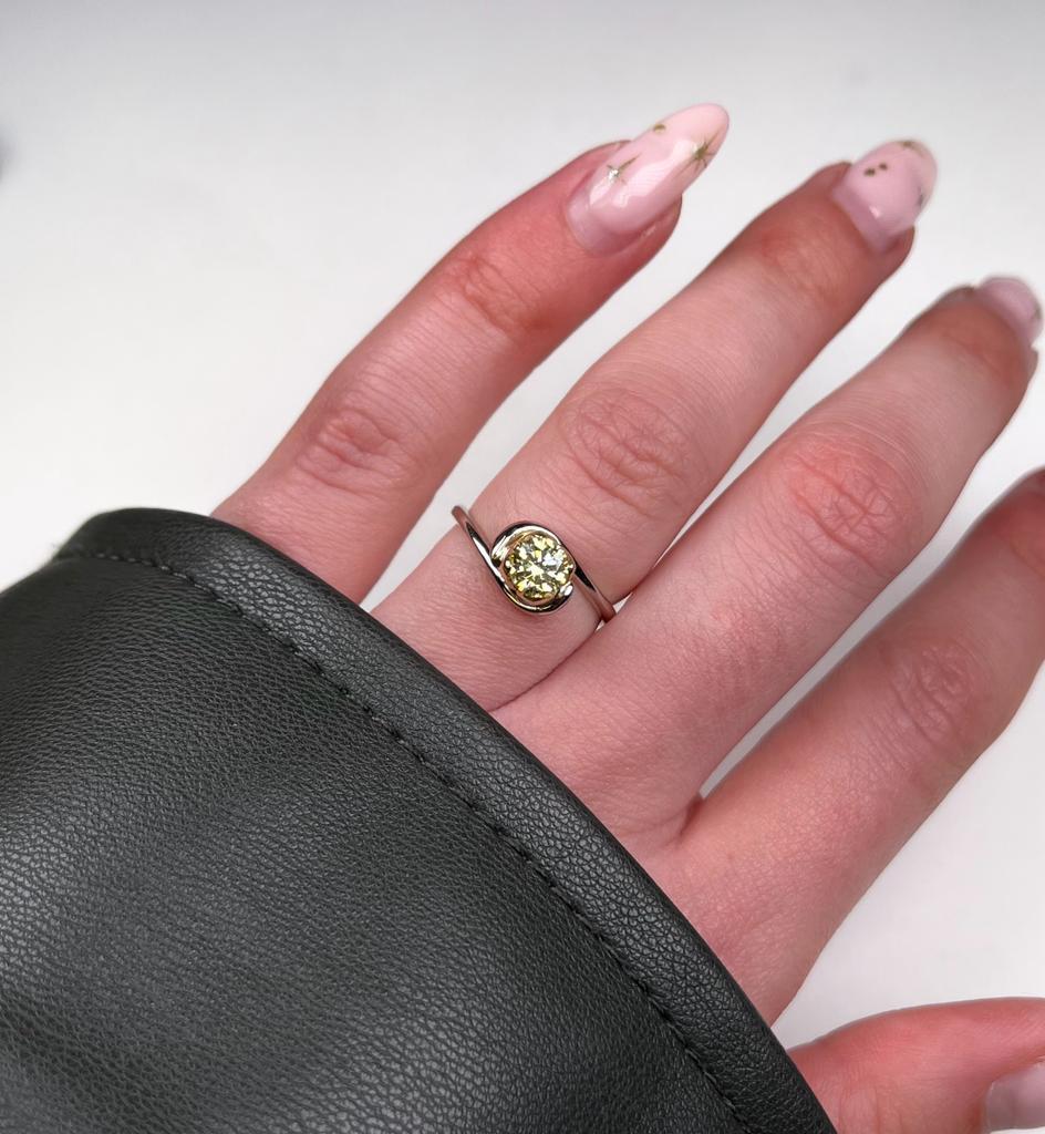 An 18ct white gold simple fine band with contrasting four petal setting in 18ct yellow gold. Set with a natural yellow .51pt round, brilliant cut diamond. 