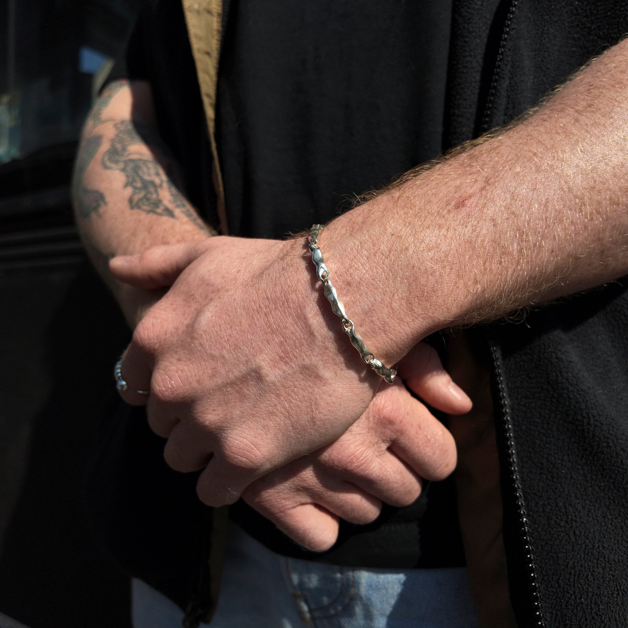 wave collection silver link bracelet on wrist with one hand holding the opposite wrist